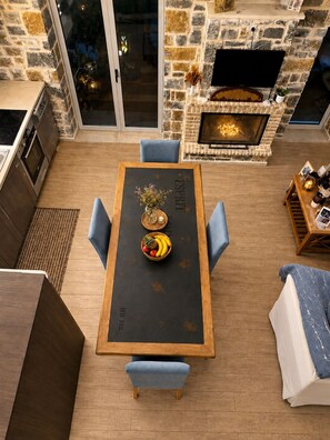 Eine moderne Küche mit Steinrückwand, ein Essbereich mit Holztisch und blauen Stühlen sowie ein Kamin.