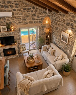 Ein gemütliches Wohnzimmer mit Steinwand, Kamin, Fernseher und Blick auf einen Pool.