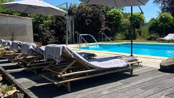 Ein Poolbereich mit Liegestühlen, Sonnenschirmen, einem Pool und einer Holzterrasse.