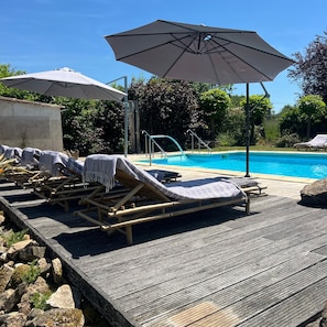 Zona junto a la piscina con sillones de descanso y sombrillas, una piscina y una terraza de madera.