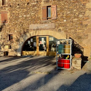 Ein Steinhaus mit einem Schild, auf dem 'Boulangerie' steht, und einem Metallgestell mit Behältern davor.