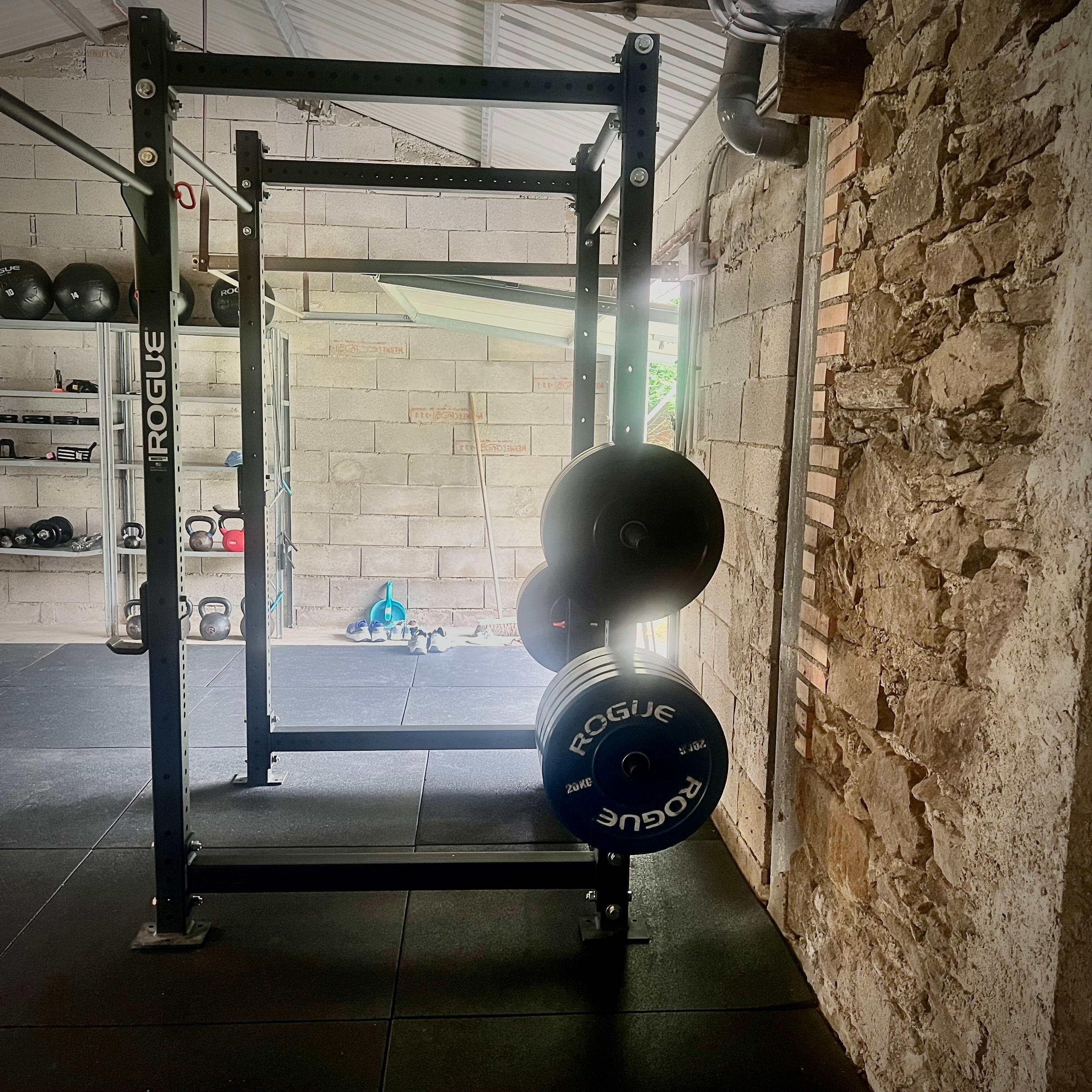 Uma área de musculação com suporte para agachamento, barras e anilhas.