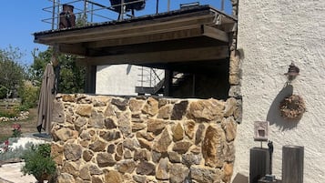 A stone wall with a balcony, a hanging flower basket, and a small potted plant.