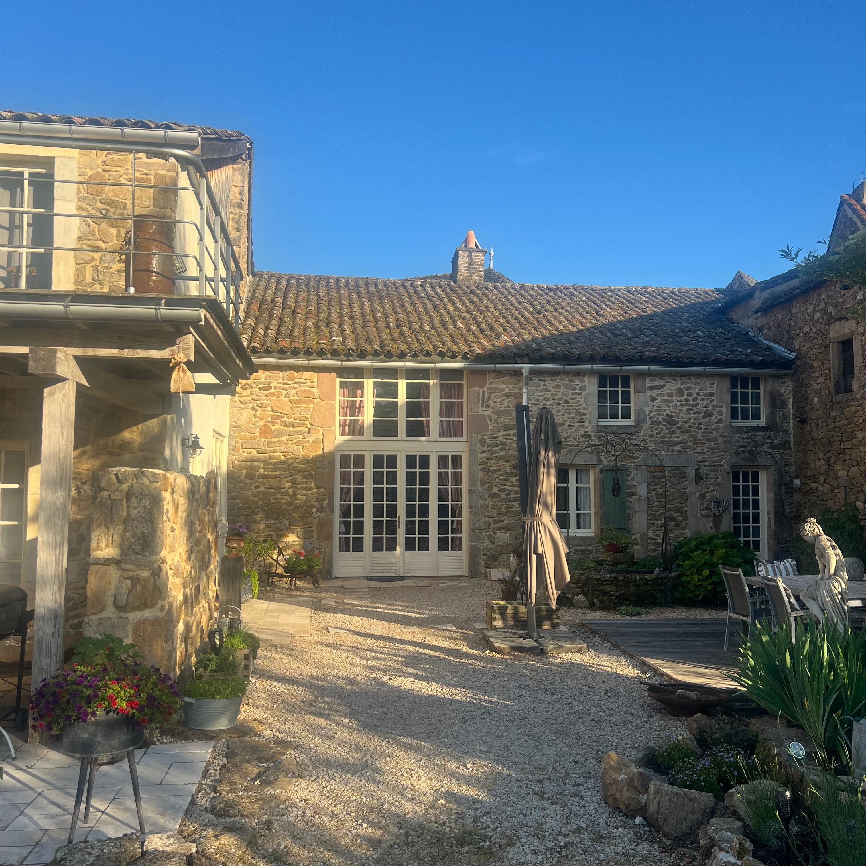 A stone house with a tiled roof, a gravel driveway, and outdoor seating.