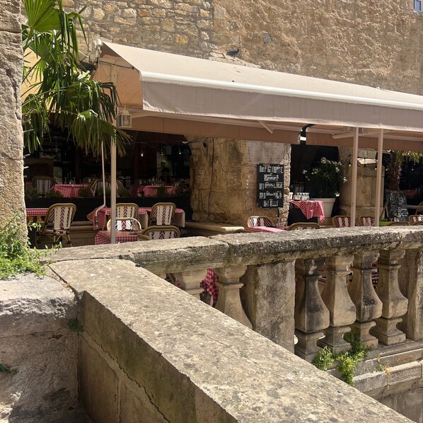 An outdoor café with stone tables and chairs, a stone balustrade, and a menu board.