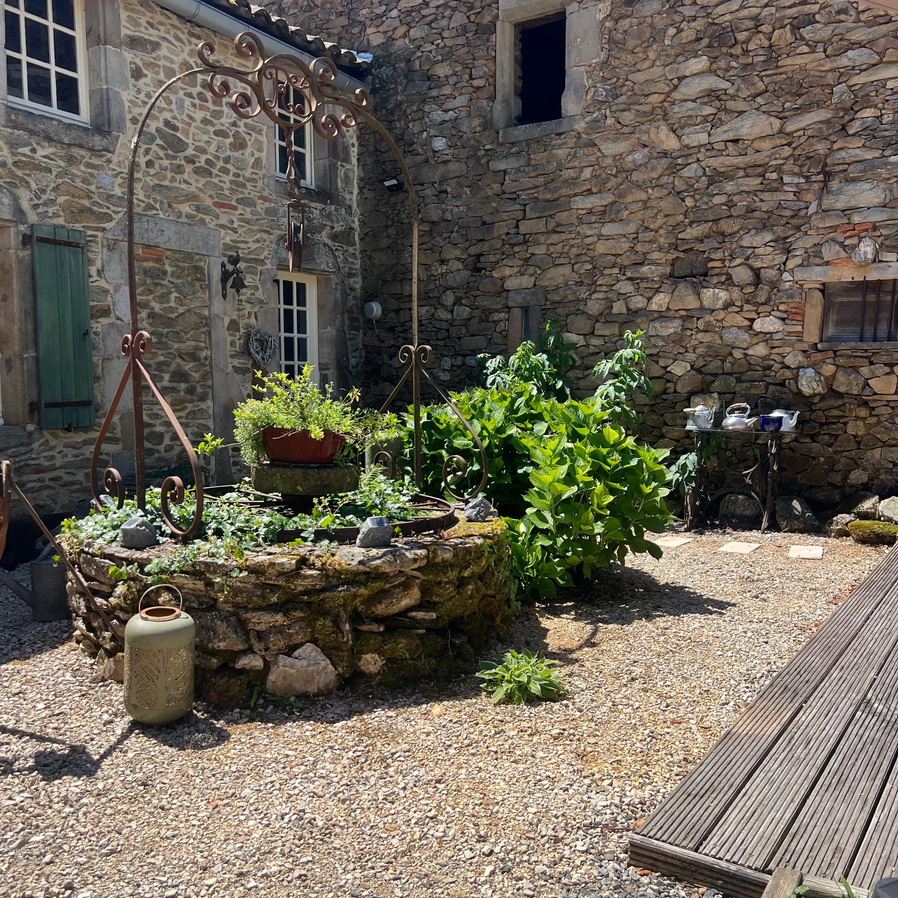 A stone building with a rustic garden, including a metal trellis and potted plants.
