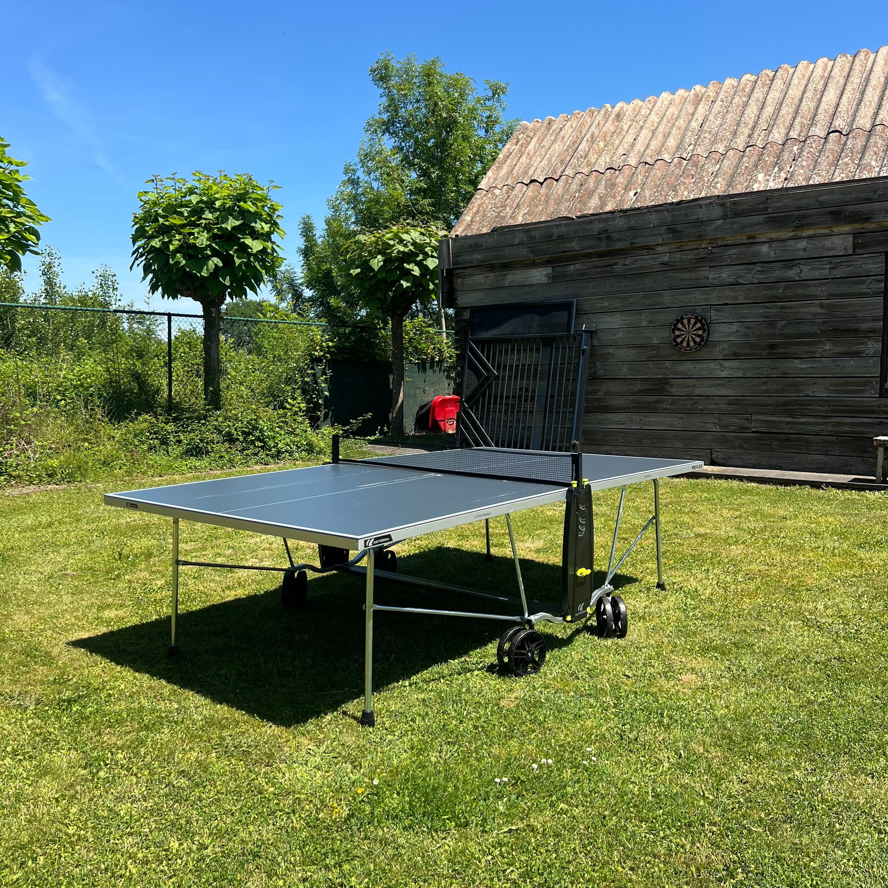Un tavolo da ping pong portatile in una zona erbosa, con un edificio in legno sullo sfondo.