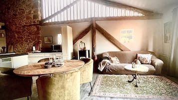 Et hyggeligt loftrum med spiseplads, sofa og et køkken i baggrunden.
