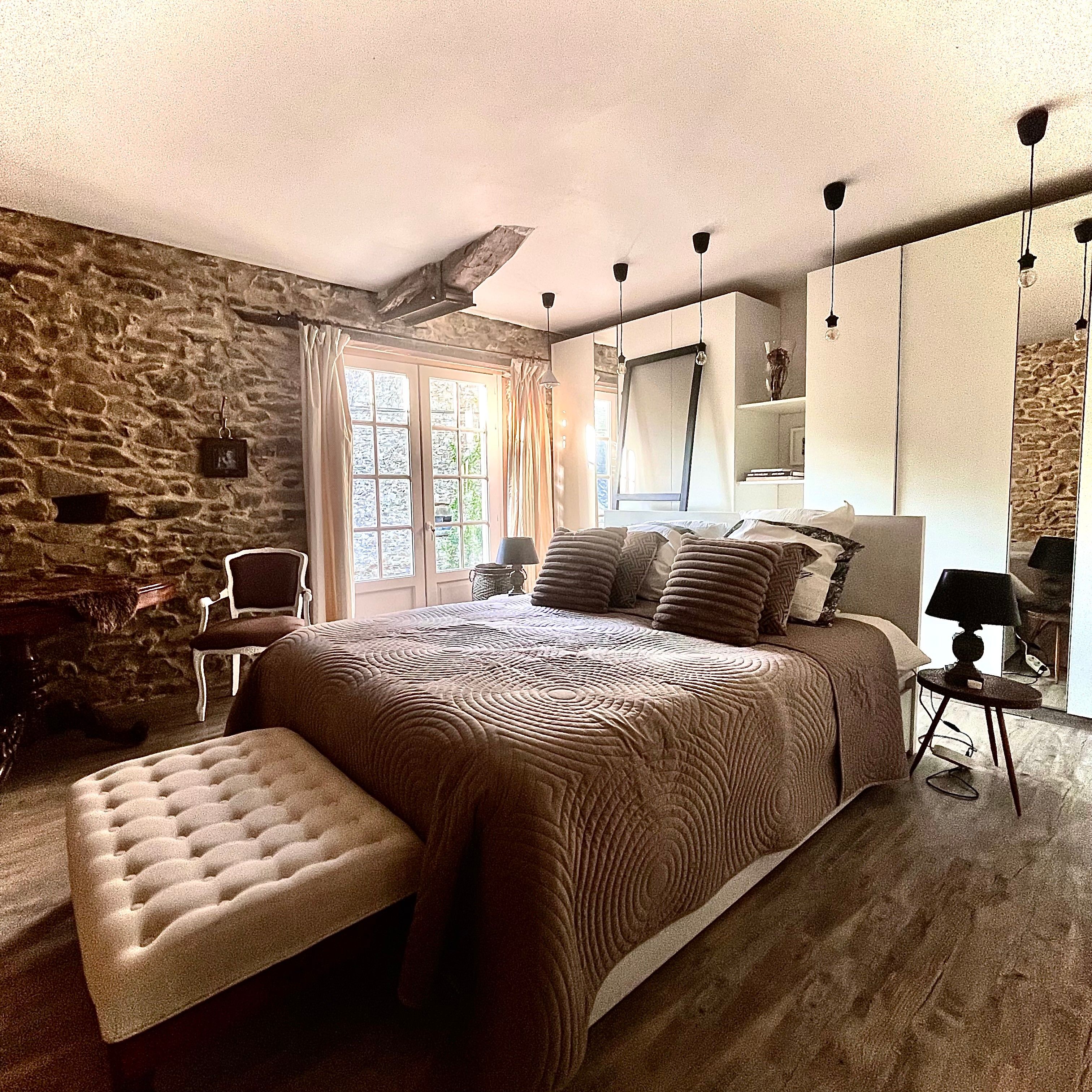 Ein Schlafzimmer mit einer Steinwand, einem großen Bett mit gemustertem Überwurf, einer Bank und einem Nachttisch mit Lampe.