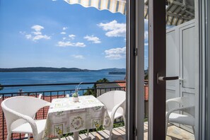 A balcony with a table and chairs, overlooking a body of water and distant land. - A2 apartment with shared pool & balcony, next to the beach (Mastrinka)