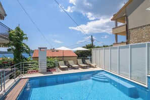 A swimming pool with lounge chairs and a view of a building with a red-tiled roof. - A2 apartment with shared pool & balcony, next to the beach (Mastrinka)