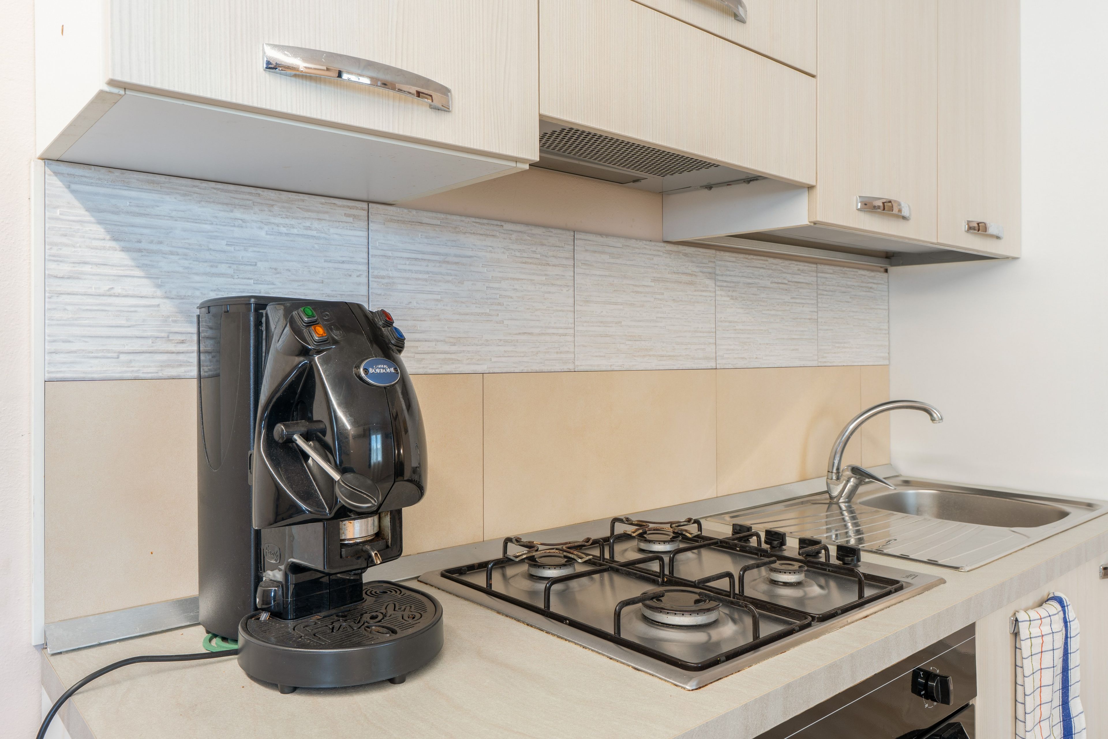 A kitchen with a coffee maker, a gas stove, and a stainless steel sink.
