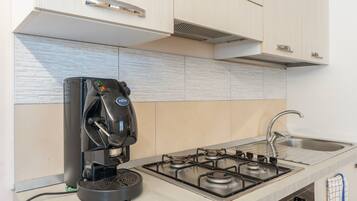 A kitchen with a coffee maker, a gas stove, and a stainless steel sink.