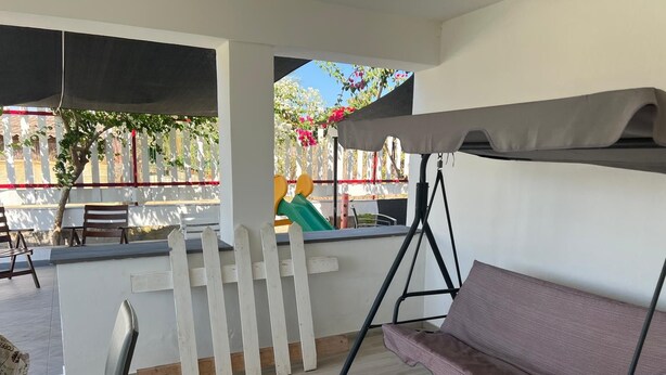 En terrasse med hvidt stakværk, en gyngestol, et polstret bænke og udsigt til en legeplads.