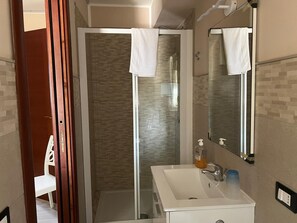 Un bagno con doccia vetro, lavandino bianco e specchio.