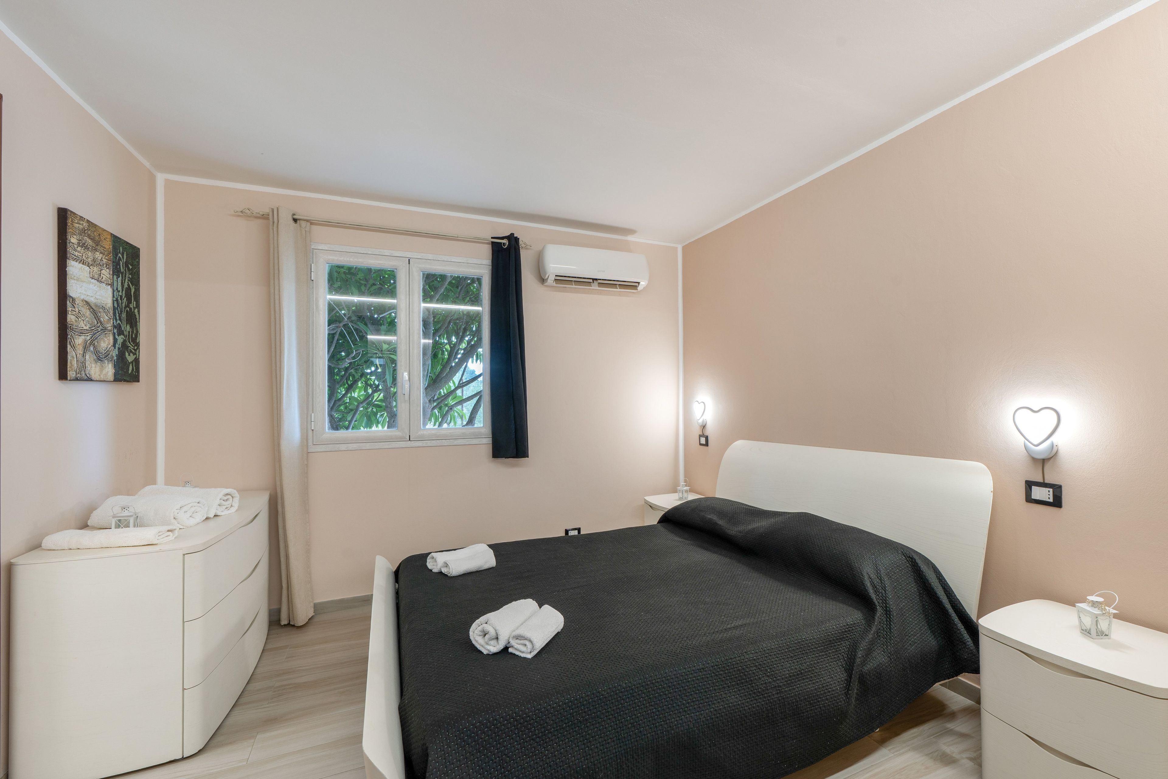 Een slaapkamer met een bed, nachtkastje, gordijnen en een airconditioning.
