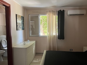 Una camera da letto con un letto, una finestra con tende, un condizionatore d'aria e un bagno con il water e un lavandino.