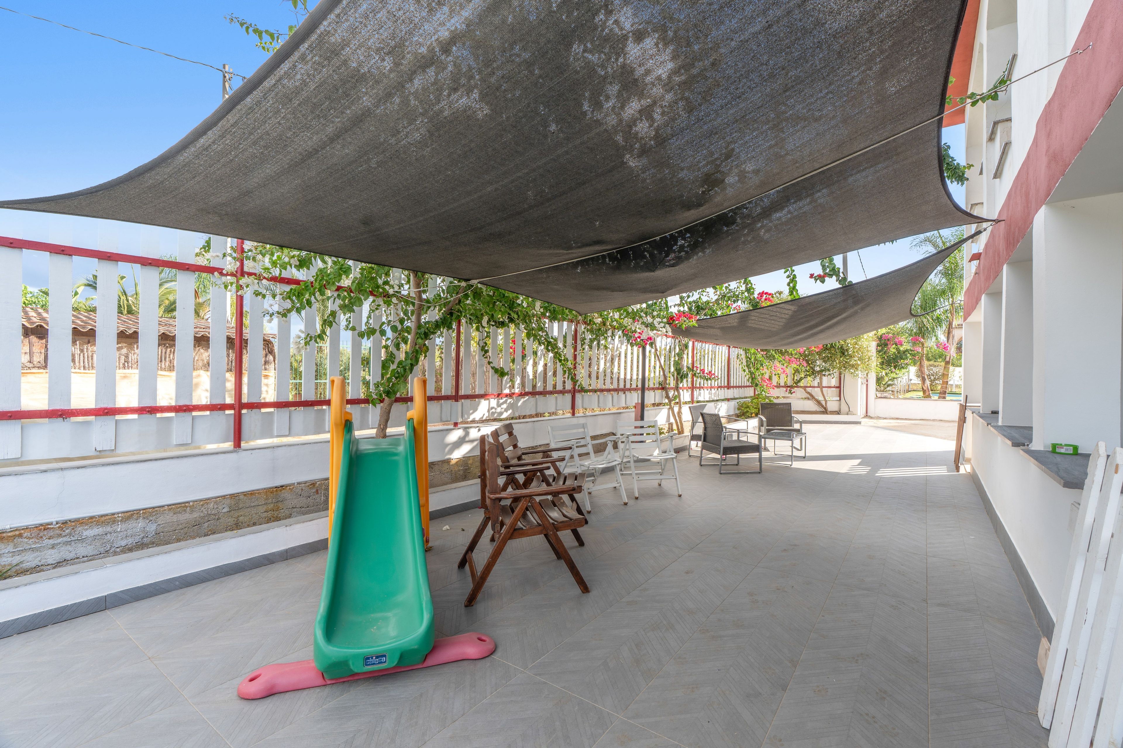 An outdoor patio area with a children's slide, seating arrangements, and a shaded canopy.