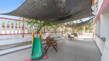 An outdoor patio area with a children's slide, seating arrangements, and a shaded canopy.