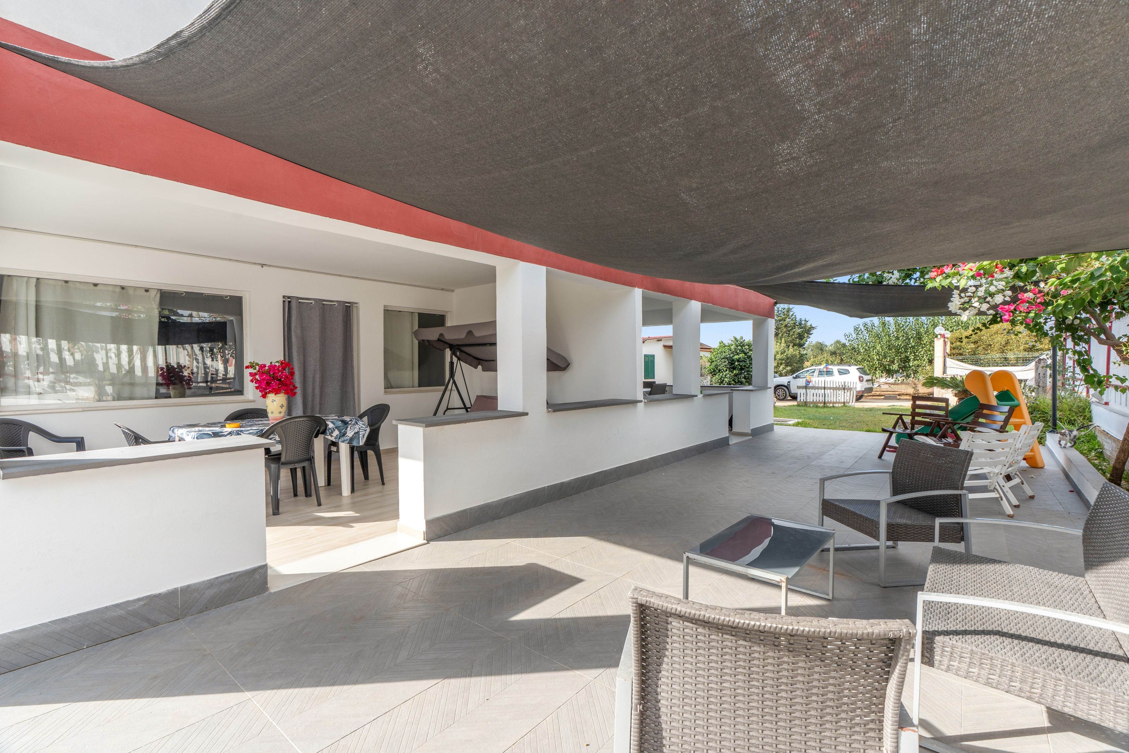 A covered outdoor area with a dining table, chairs, and a seating arrangement.