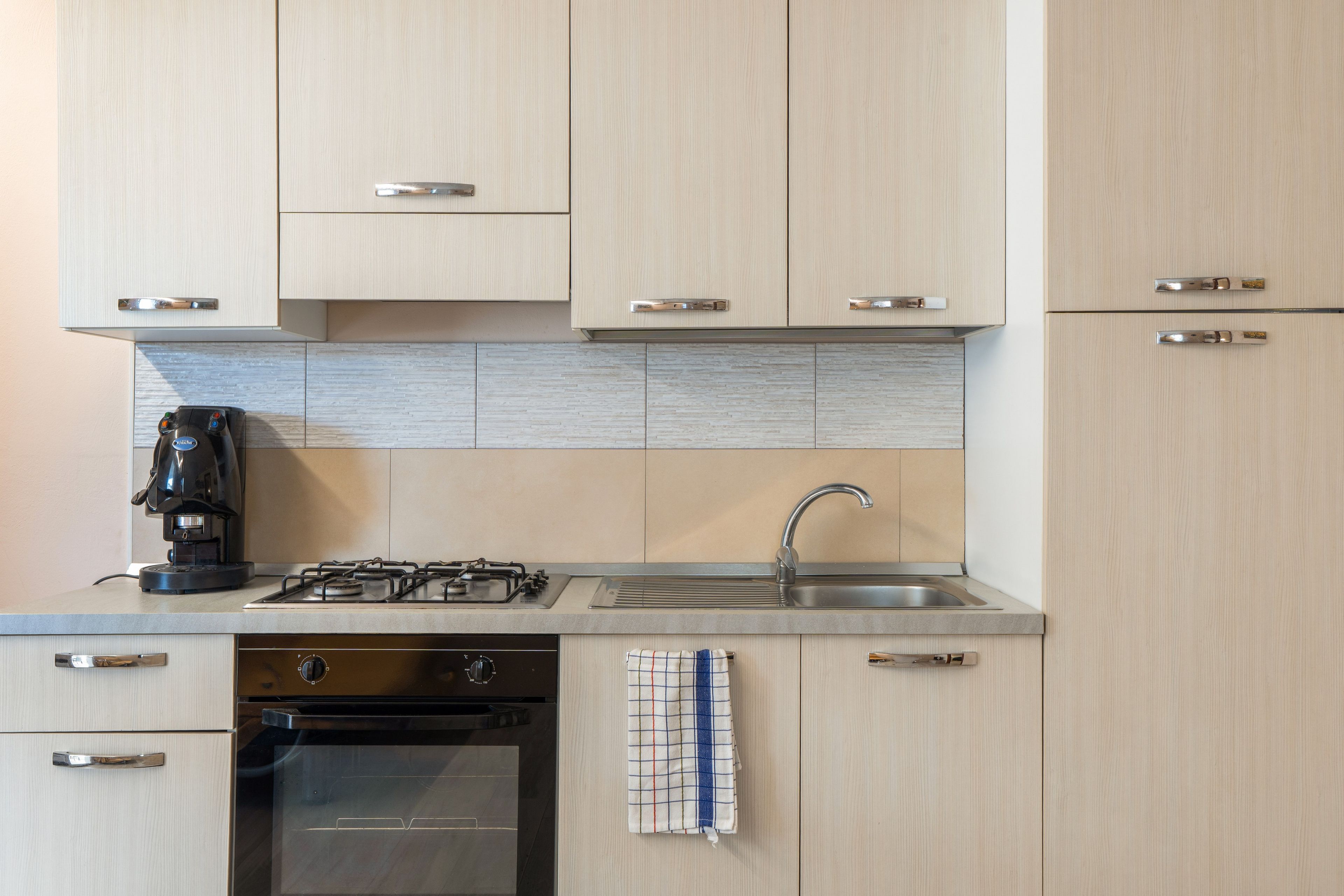 A modern kitchen with a gas stove, a coffee maker, a sink, and a towel hanging on the wall.