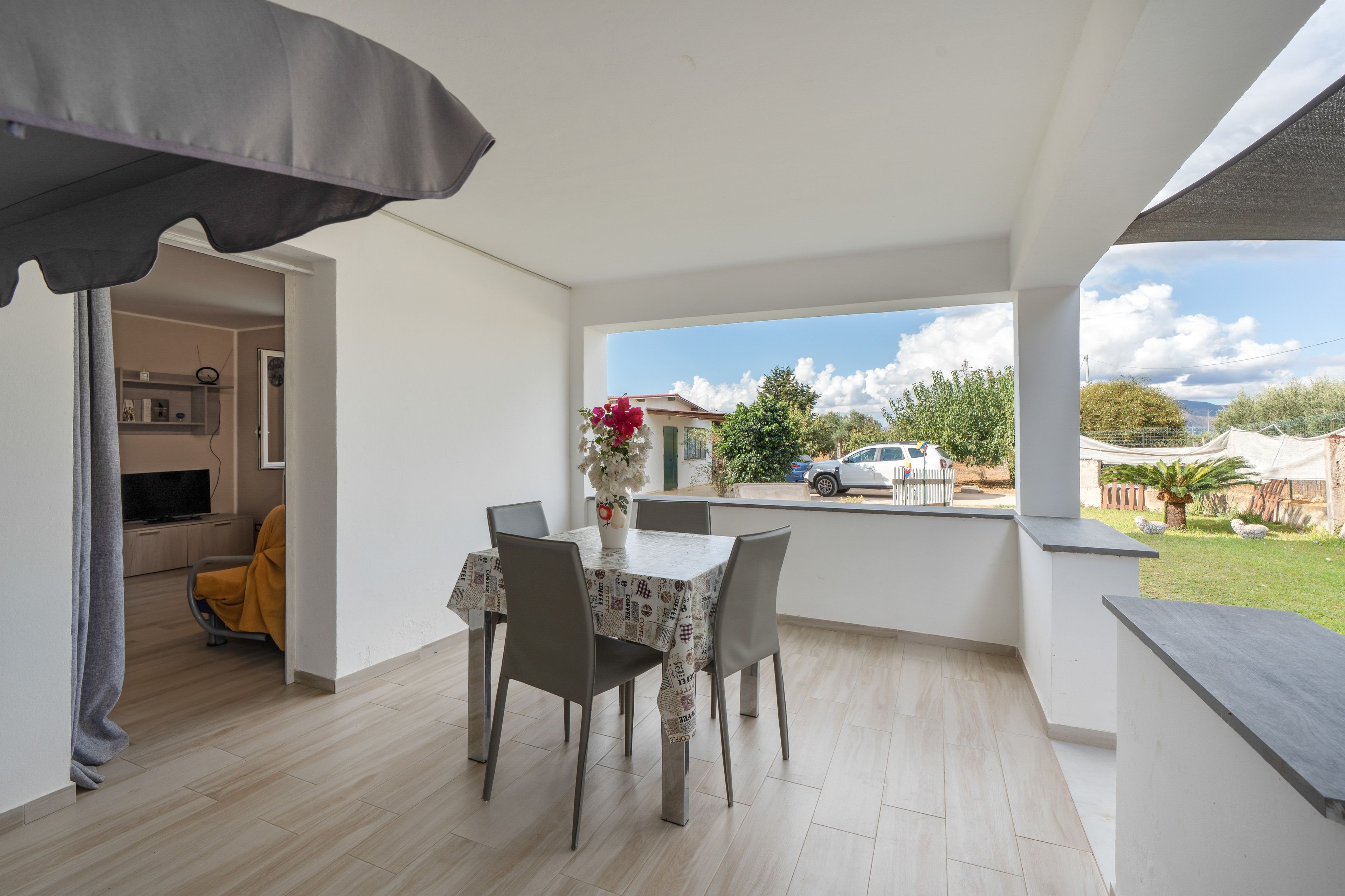 A dining area with a table and chairs, a vase with flowers, and a view of the outside.