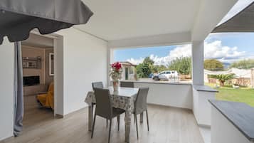 A dining area with a table and chairs, a vase with flowers, and a view of the outside.