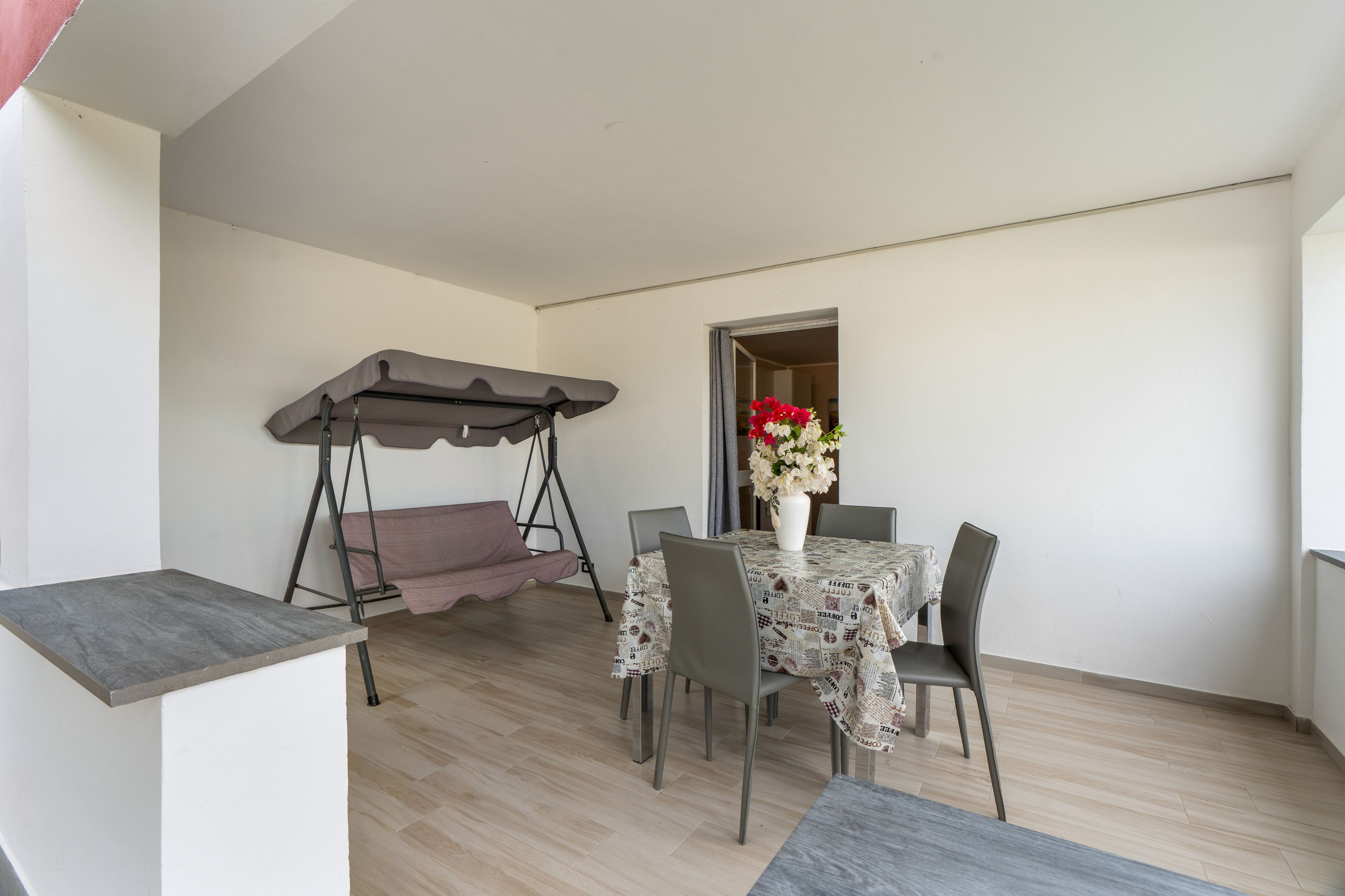 A small dining area with a table, chairs, a swing, and a vase of flowers.
