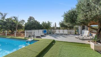 A pool area with a clear blue pool, surrounded by a white fence, and equipped with white lounge chairs.
