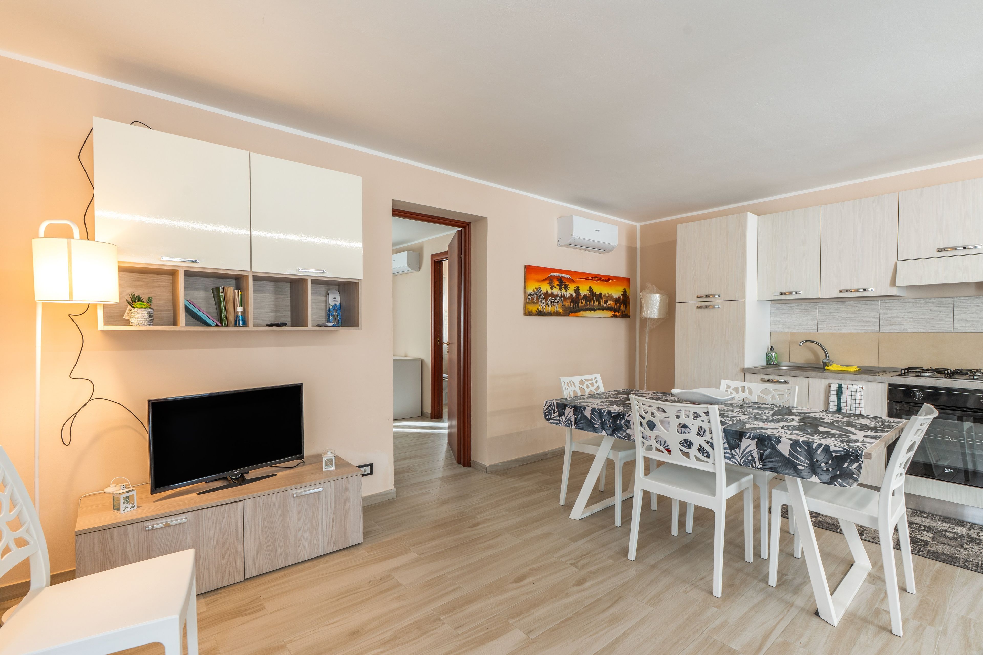 A modern kitchen with white cabinets, a dining area with a table and chairs, and a television on a wooden stand.