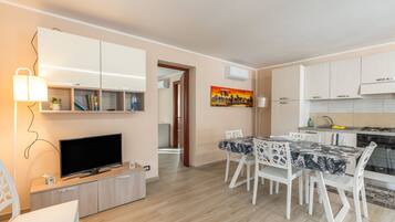 A modern kitchen with white cabinets, a dining area with a table and chairs, and a television on a wooden stand.