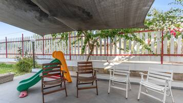 A covered outdoor seating area with a children's slide, benches, and a white picket fence.