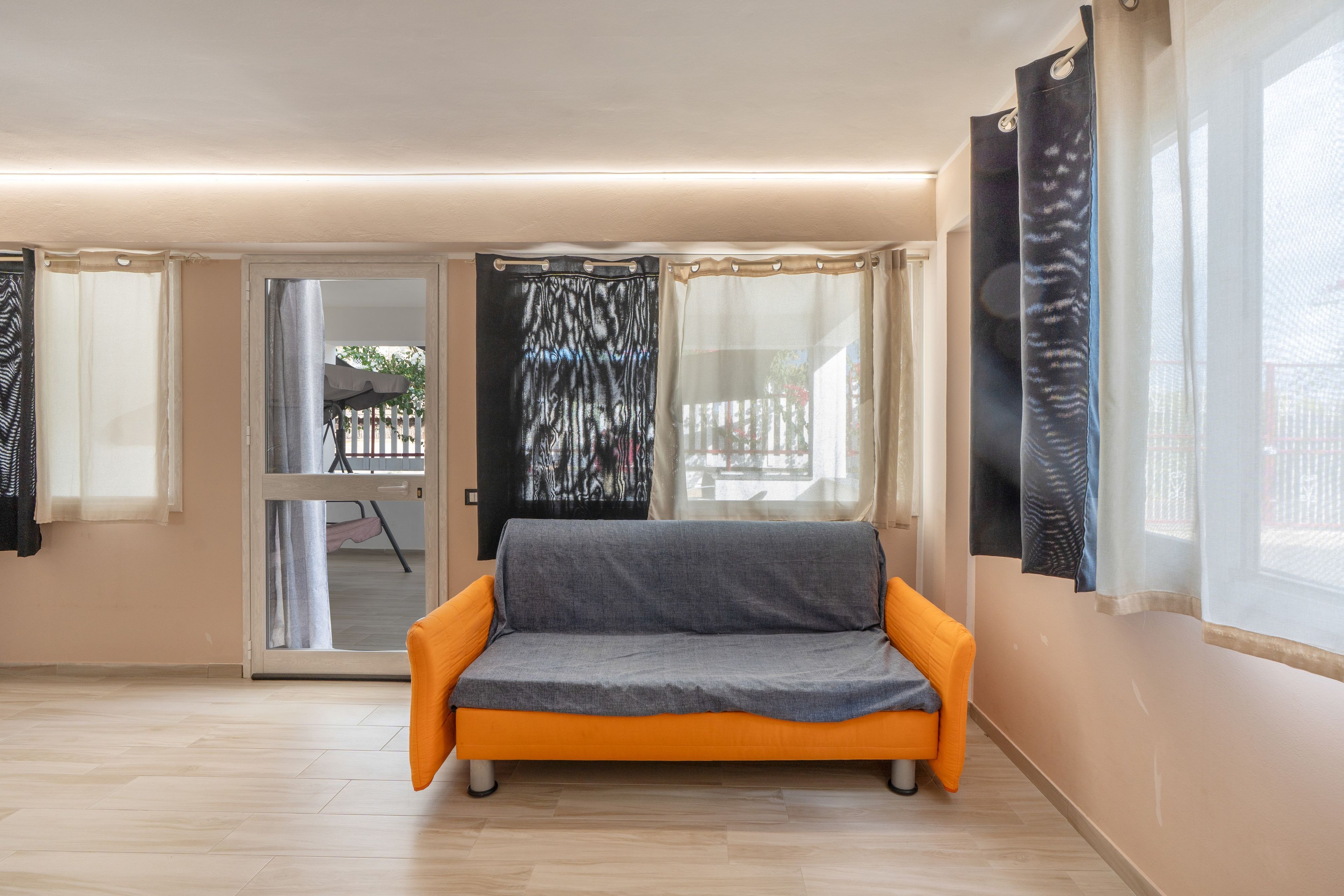Ein Zimmer mit einer Couch, einer Glasschiebetür, die zu einem Außenbereich führt, und einem Fenster mit Vorhängen.