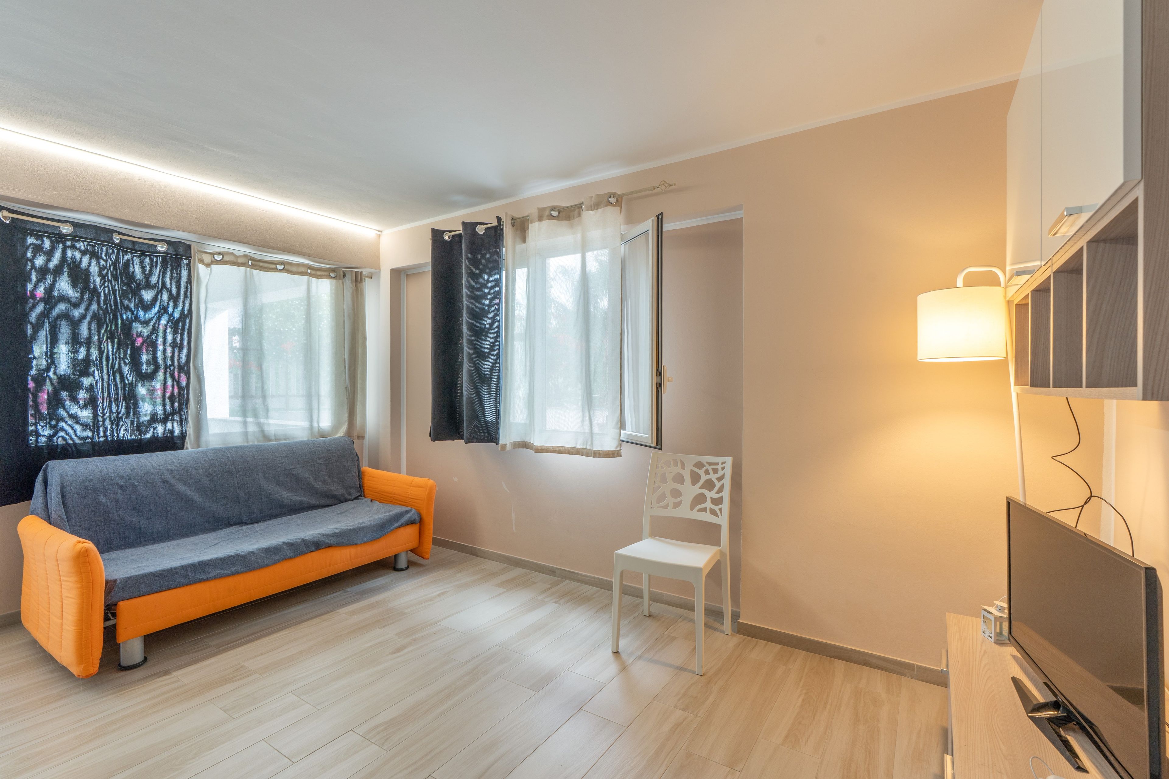A room with a sofa, a chair, a TV, and a window with curtains.