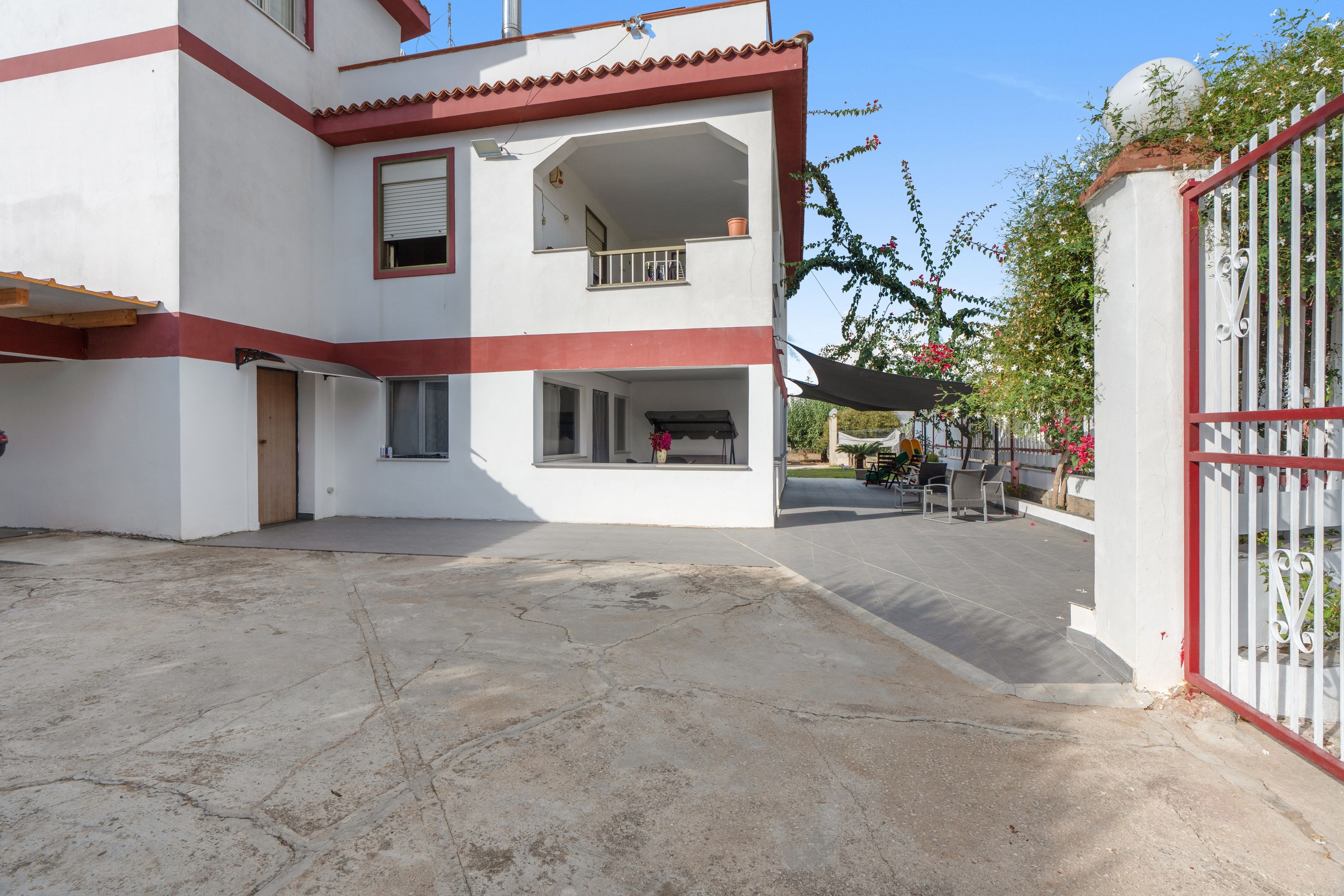 Un edificio a due piani con un balcone, un ingresso chiuso da cancello e un cortile pavimentato.