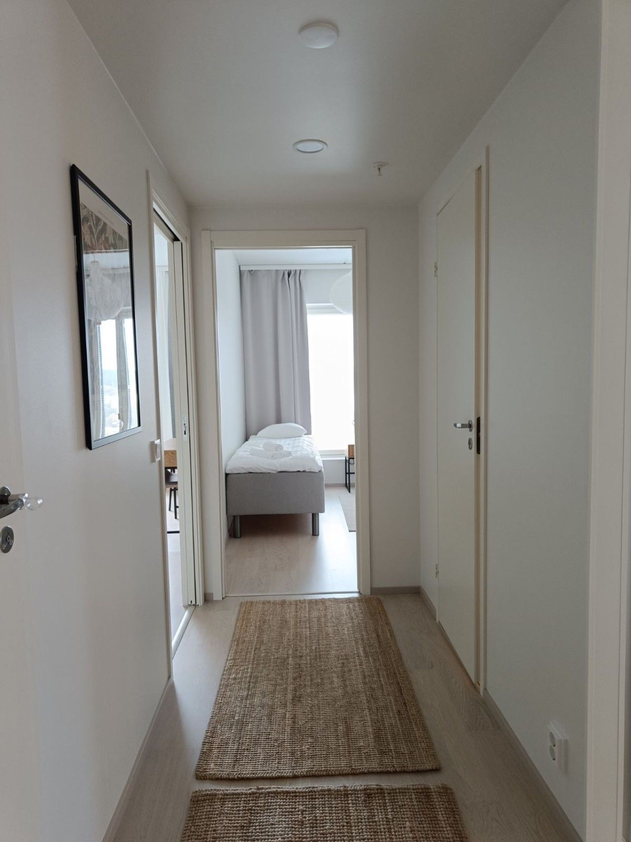 Un pasillo estrecho que conduce a un dormitorio con una cama, una puerta a la izquierda y otra a la derecha.