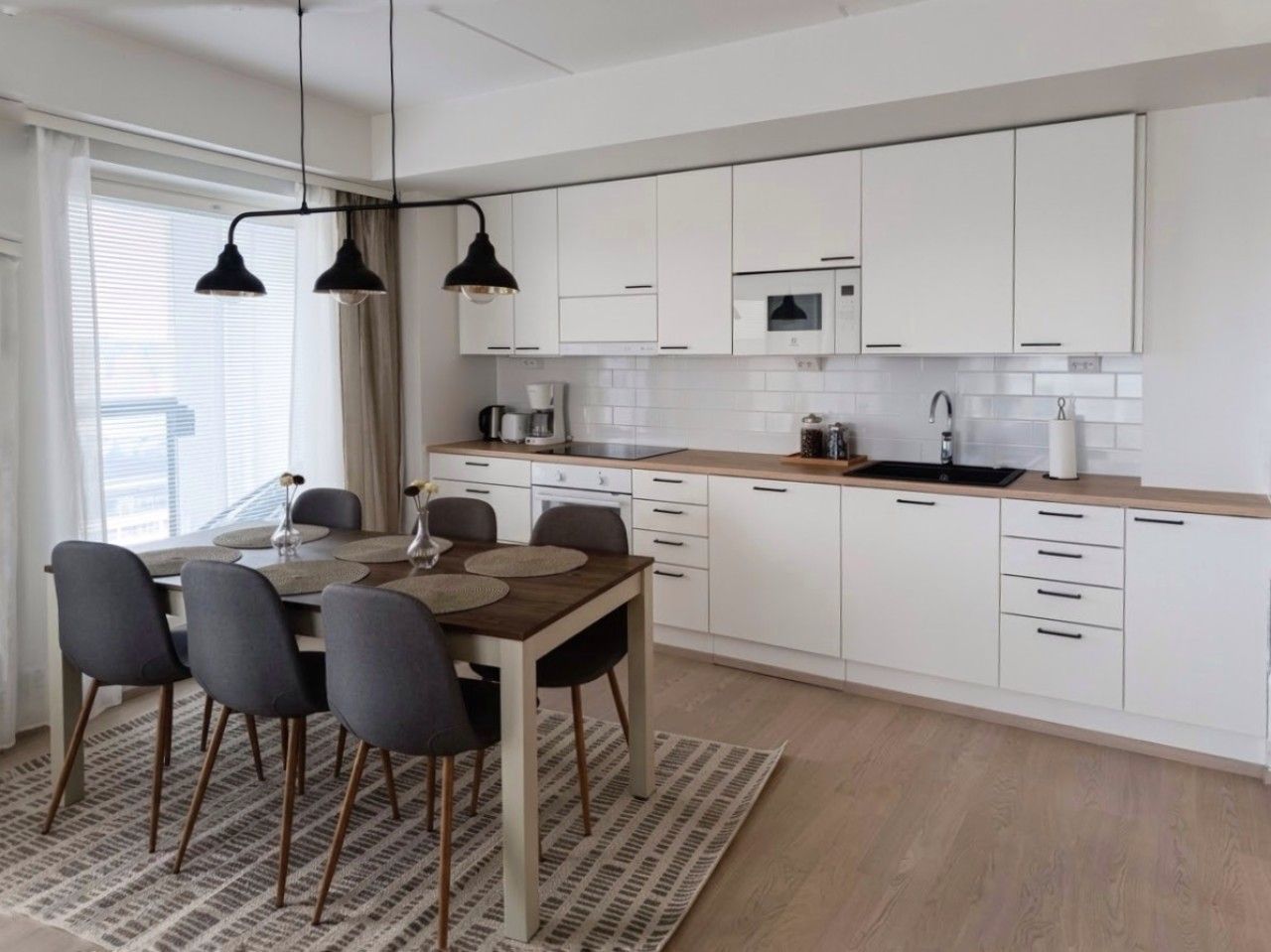 Una cocina moderna con armarios blancos, encimera de madera y comedor con mesa y sillas.