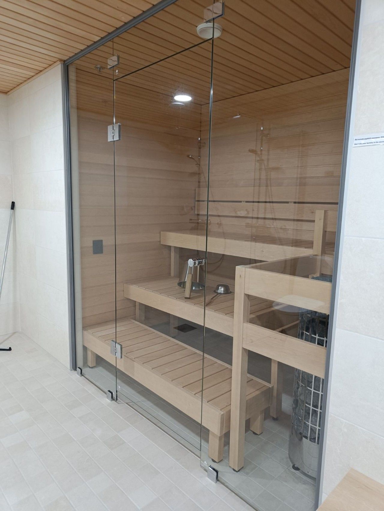 A glass-enclosed sauna with wooden shelves and a metal basin.