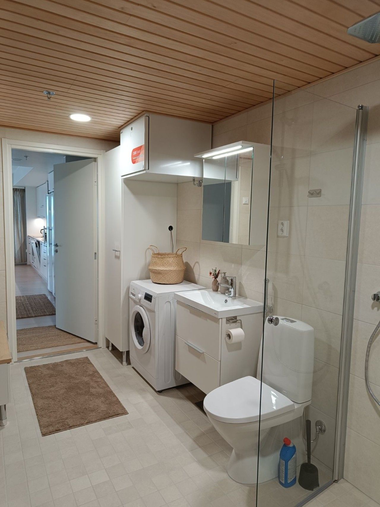 A compact bathroom with a washing machine, a toilet, and a glass-enclosed shower.