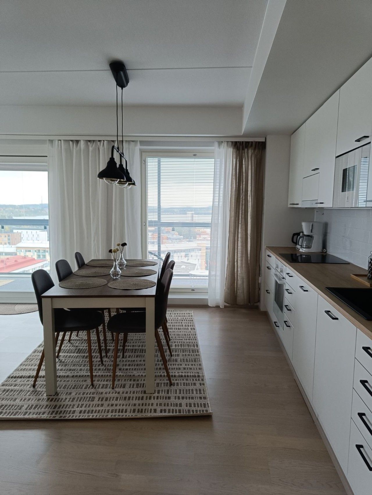 Una cocina moderna con armarios blancos, un comedor con mesa y sillas, y vistas a través del ventanal.