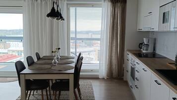 Una cocina moderna con armarios blancos, un comedor con mesa y sillas, y vistas a través del ventanal.