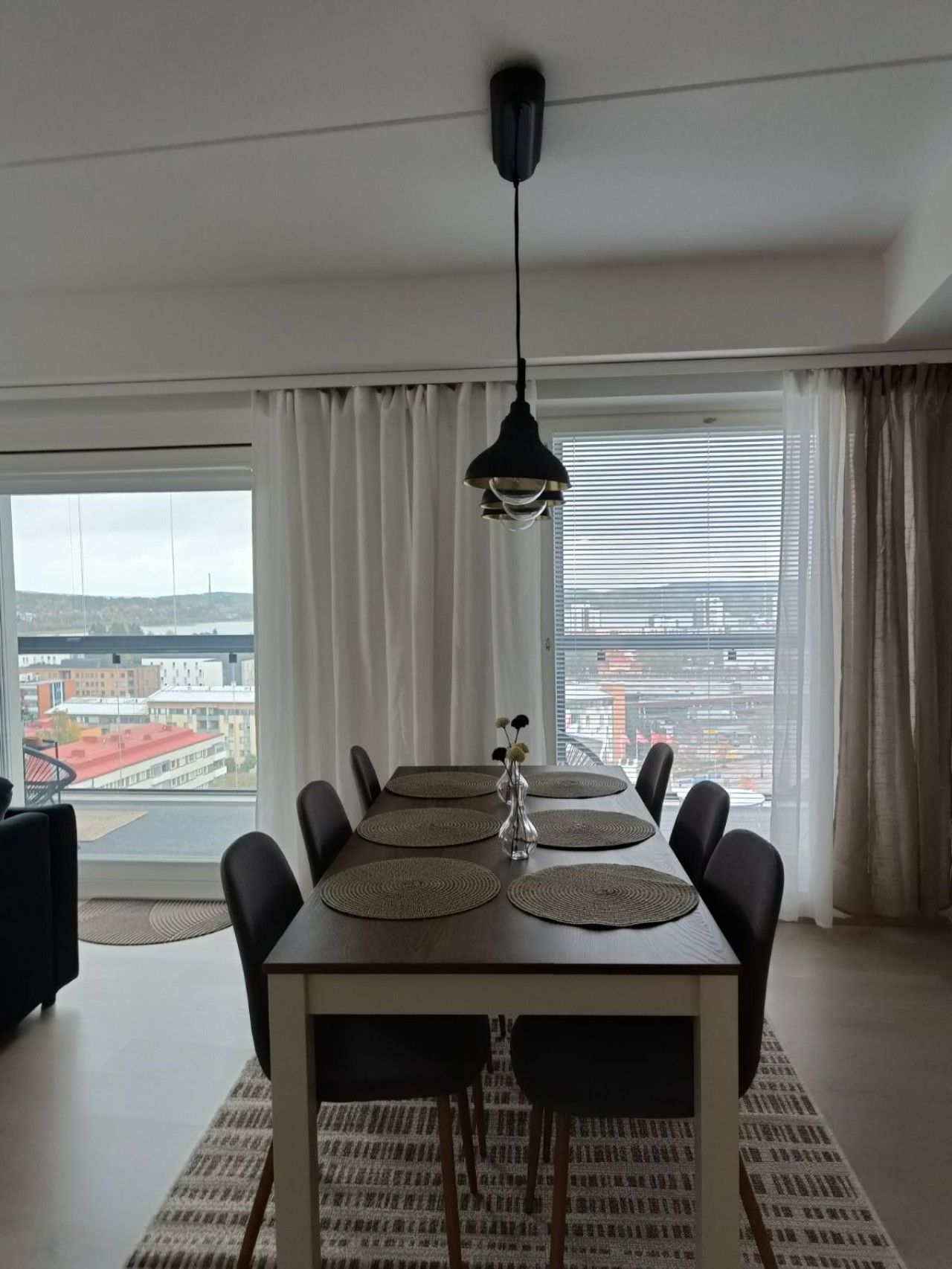 Un coin repas avec une table dressée pour six personnes, un luminaire suspendu et une vue sur la ville grâce à de grandes fenêtres.