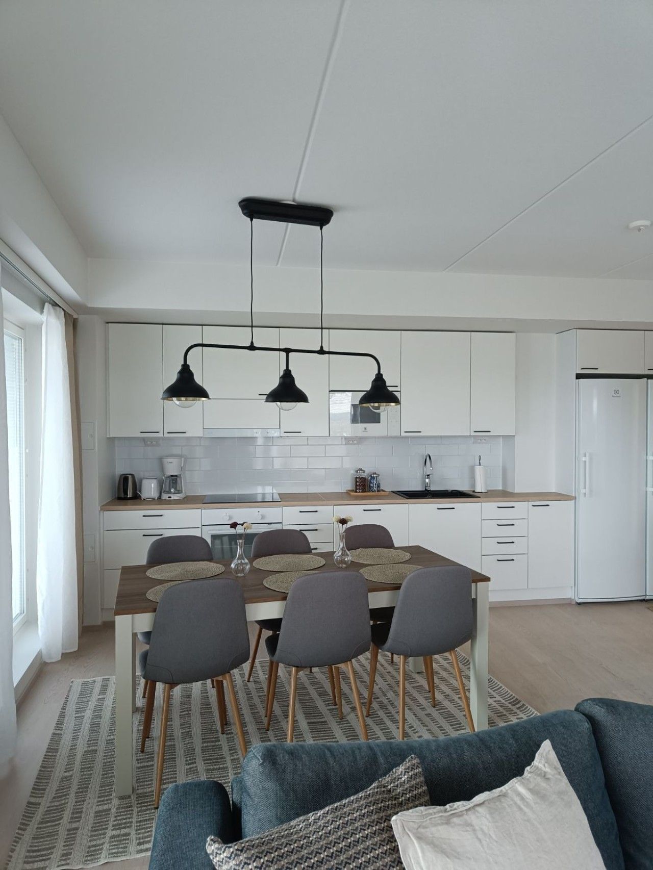 Una cocina moderna con armarios blancos, una isla central con taburetes e iluminación colgante.