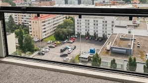 Näkymä ikkunasta, josta avautuu näkymä parkkipaikalle, jonka takana kohoavat rakennukset ja kauempana näkyy vesistö.