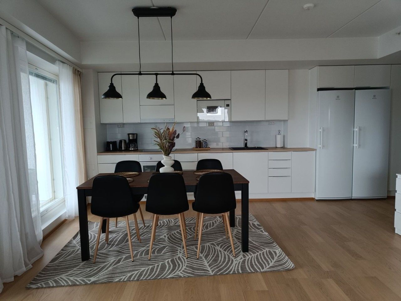 Une cuisine moderne avec des meubles blancs, une table à manger avec des chaises et un réfrigérateur.