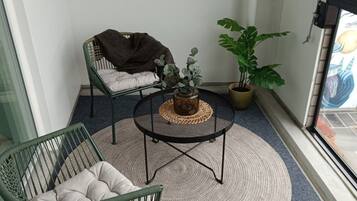 A balcony with a green chair, a small round table with a woven mat, and a potted plant.