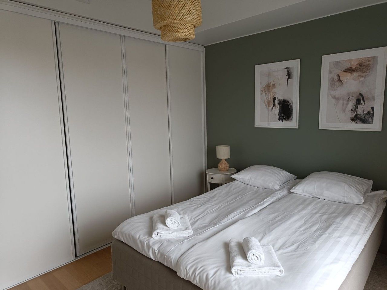 A bedroom with a bed, two pillows, a nightstand, a lamp, and artwork on the wall.