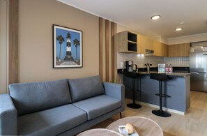 A modern living room with a grey sofa, a kitchen area with wooden cabinets, and a bar stool. - w Charming Loft w Balcony in Prime Miraflores (Lima)