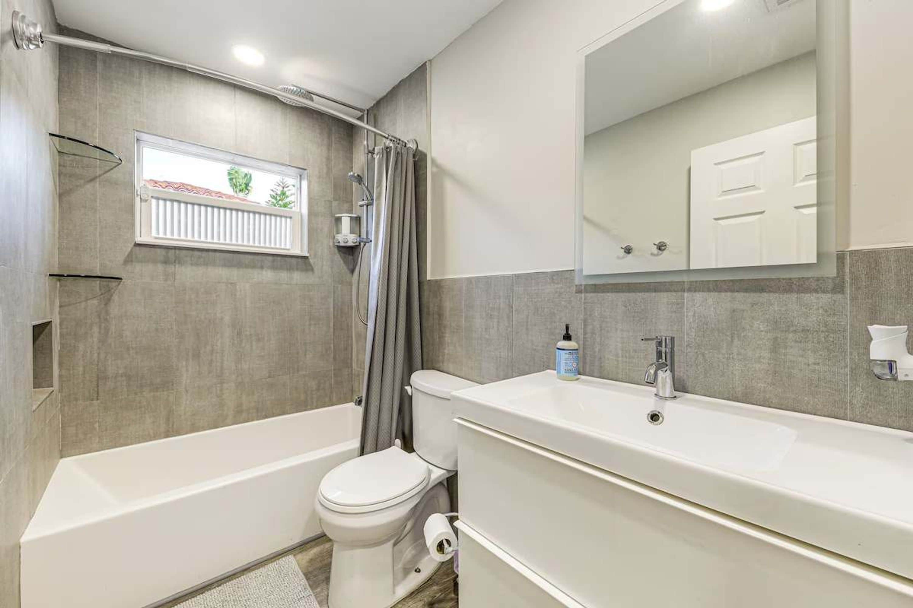 A bathroom with a bathtub, toilet, and a large mirror above the sink.