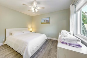 A hotel room with a bed, a ceiling fan, a painting, a window with towels, and a nightstand with a lamp. - Beach in 5 Mins - Private Saltwater Pool BBQ (Deerfield Beach)